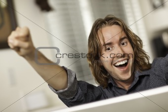 Happy Young Man Using A Laptop Computer and Cheering with Fists in the Air.