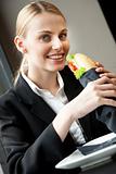 young smiling businesswoman eating a sandwich and looking at camera