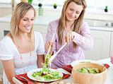 Two delighted women eating salad in the kitchen