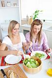 Two glowing female friends eating salad in the kitchen