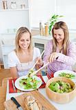 Two merry female friends eating salad in the kitchen