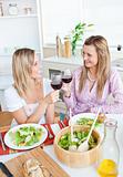 Two cheerful female friends eating salad in the kitchen