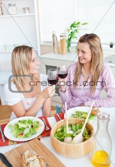 Two cheerful female friends eating salad in the kitchen