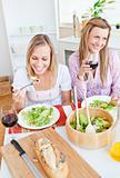 Two delighted female friends eating salad in the kitchen