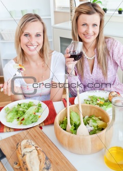 Two positive female friends eating salad in the kitchen