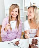 Joyful female friends eating a chocolate cake and drinking in th