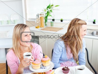 Two laughing female friends eating pastries and drinking coffee 