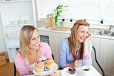 Two cheerful female friends eating pastries and drinking coffee 