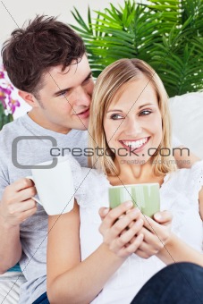 handsome man whispering something to his girlfriend while drinki