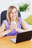 Smiling woman holding a glass of water behind her laptop