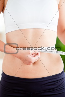 Hispanic woman measuring her waist with a tape in the living-roo