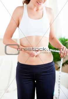Thin hispanic woman measuring her waist with a tape in the livin