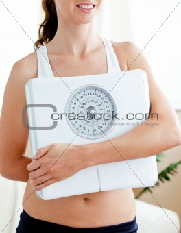Close-up of a fit hispanic woman holding a scale in her living-r