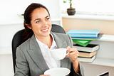 Cheerful hispanic businesswoman drinking coffee at her desk