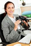 Smiling hispanic businesswoman holding binoculars sitting at her