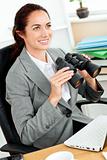 Radiant hispanic businesswoman holding binoculars sitting at her