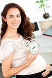 Radiant pregnant businesswoman holding an alarm clock and sittin