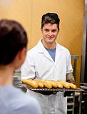 Glowing young male baker holding baguettes in the kitchen