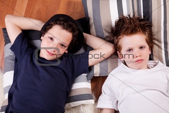 two boys lying on the floor with his head resting on two pillows