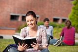 Cute female student reading a book sitting on grass