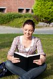 Relaxed female student reading a book sitting on grass