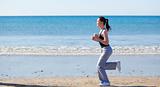 Sporty woman running on the beach and listening to music