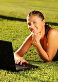 Pretty young girl working on her laptop on the grass