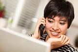 Pretty Smiling Multiethnic Woman with Cell Phone and Using Her Laptop.