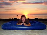 The joyful guy on a mattress on a background of a sunset