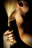 Abstract dramatically lit image of woman's shoulder, back and blond hair with male hand gripping her lock.