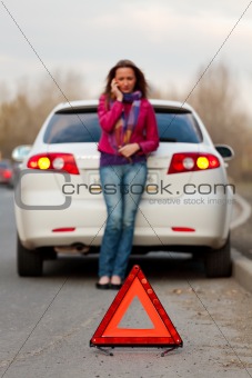 Woman calls to a service standing by a white car. 