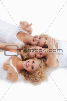 three young women lying on the floor, looking up, showing thumbs up