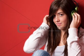 Young girl listening to music with headphones on a red wall