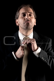 businessman tie fastening, overwhelmed expression on black background