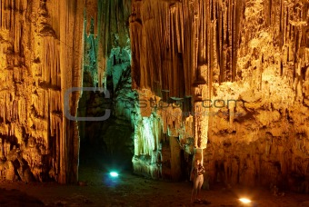 Young woman touching huge stalactites in colorful Melidoni Cave