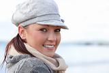 Portrait of a cute young woman with cap and scarf standing on the beach in front of the ocean