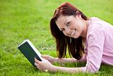 Cheerful young woman reading a book lying on the grass