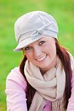 Happy young woman wearing cap and scarf smiling at the camera in a park