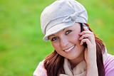 Pretty young woman wearing cap and scarf talking on phone on the grass in a park