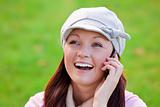 Pretty young woman wearing cap and scarf talking on phone on the grass in a park