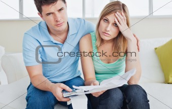 worried couple after calculating bills sitting on sofa