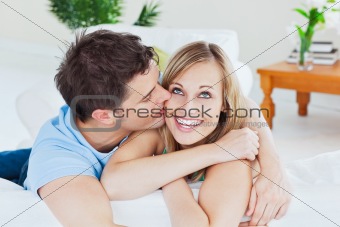 handsome man kissing his joyful girlfriend both lying on the sof