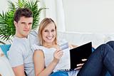 young couple with laptop and credit card bying online lying in t