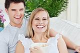 laughing couple eating pop-corn lying on the sofa in the living-