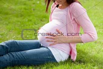 Pregnant woman holding her stomach sitting on the grass