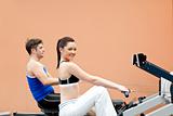 Positive woman with her boyfriend using a rower in a sport centr