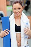 sporty woman holding bottle of water and exercice mat