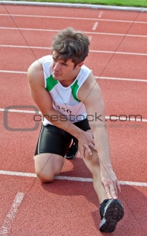 young male sprinter streching on the floor before a race in a st