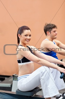 Athletic young people using a rower in a fitness center