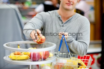 close-up of a young man putting apples in his shopping basket